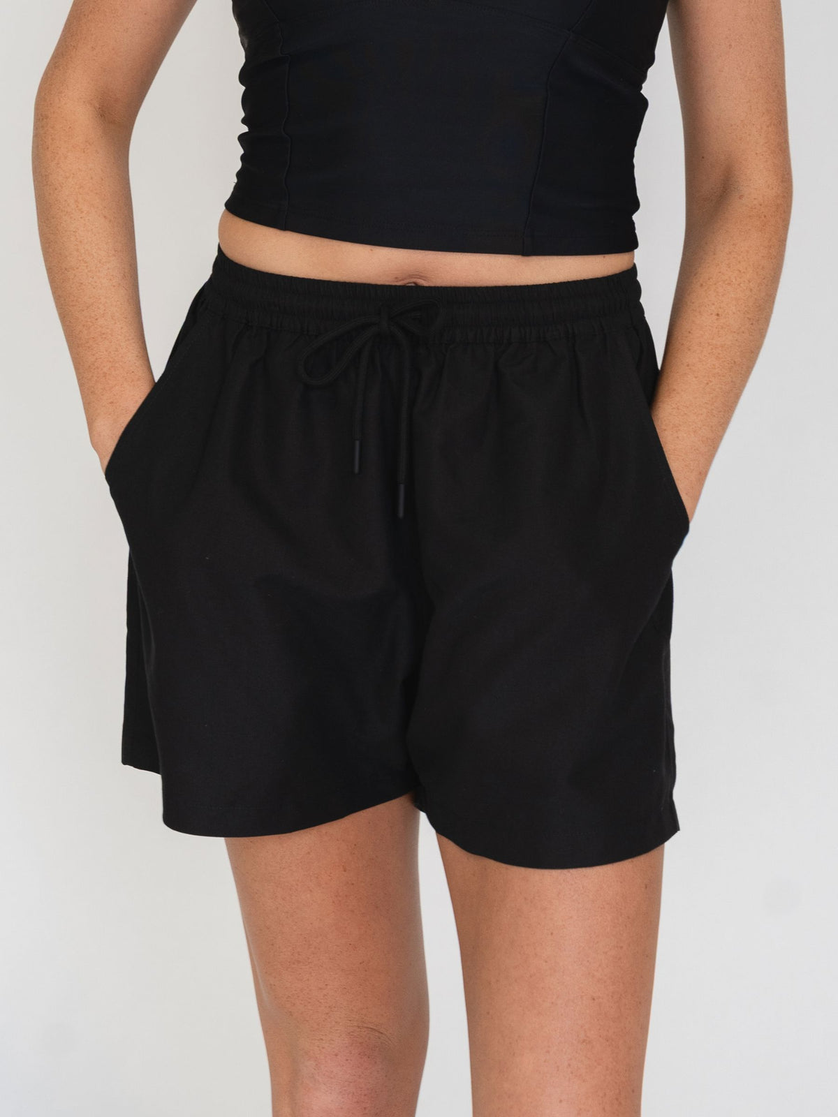 Close up of woman wearing black shorts and a black top on a white background