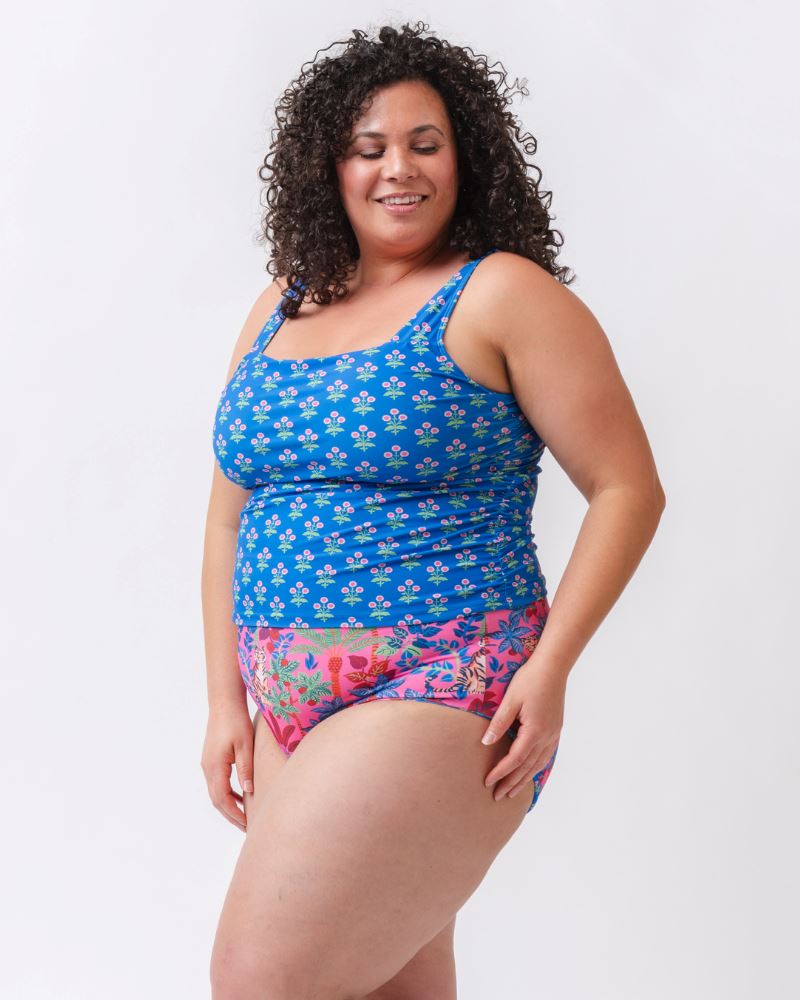 Photo of a woman from the side wearing a blue floral print square neck swim tankini with a bold pink tiger print high waist swim bottom