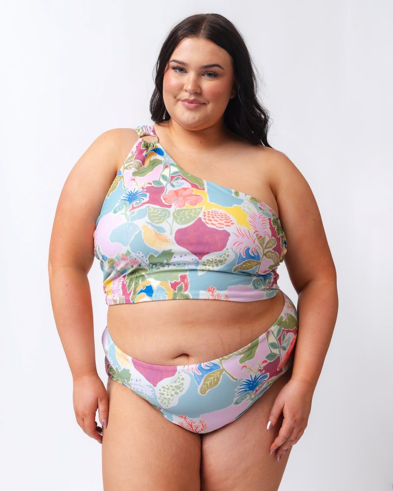 Photo of a woman wearing a colorful seashell inspired one-shoulder swim crop top and a colorful seashell inspired high waist swim bottom