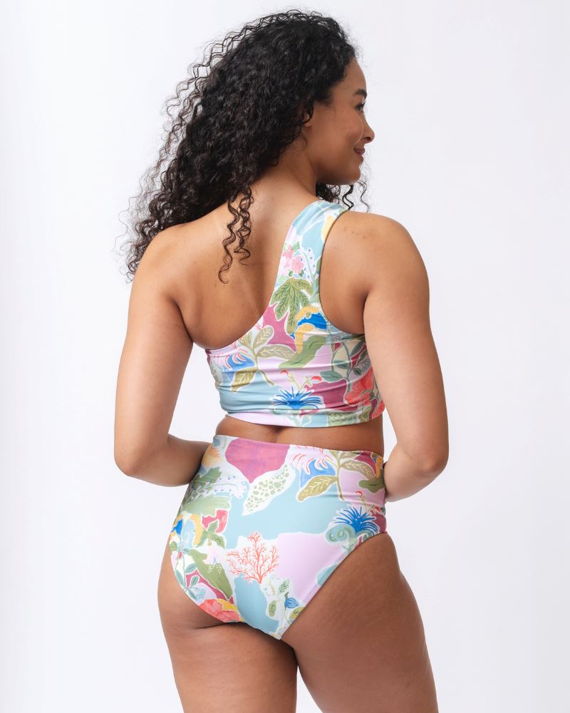 Photo of a woman wearing a colorful seashell inspired one-shoulder swim crop top and a colorful seashell inspired high waist swim bottom- back angle