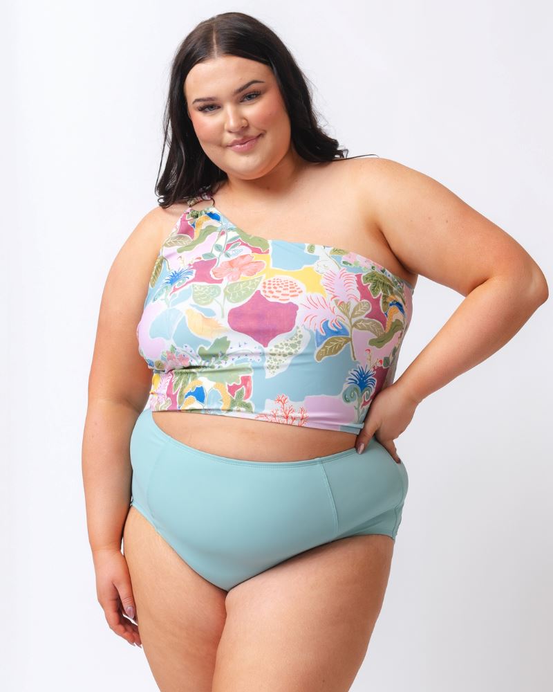 Photo of a woman wearing a colorful seashell inspired one-shoulder swim crop top and a light blue high waist swim bottom
