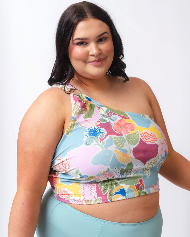 Photo of a woman wearing a colorful seashell inspired one-shoulder swim crop top and a light blue high waist swim bottom