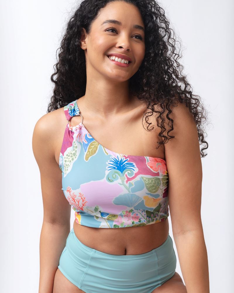 Photo of a woman wearing a colorful seashell inspired one-shoulder swim crop top and a light blue high waist swim bottom