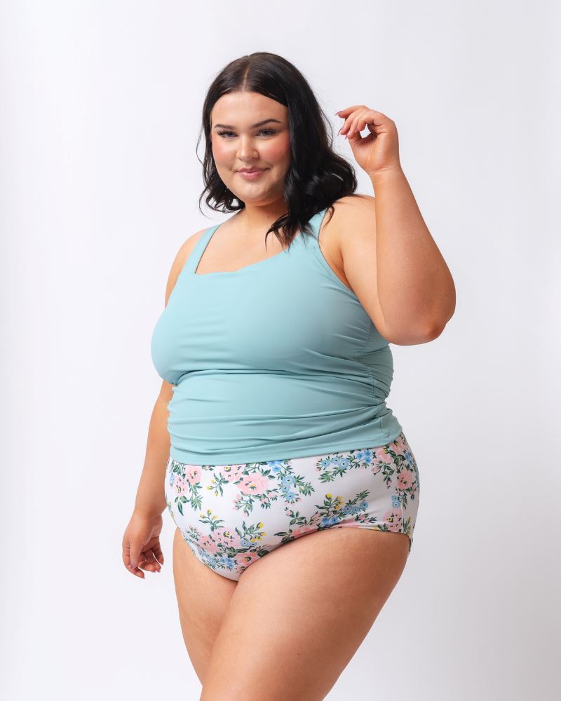 Photo of a woman wearing a light blue square neck swim tankini top and a white and pink floral swim bottom- side angle