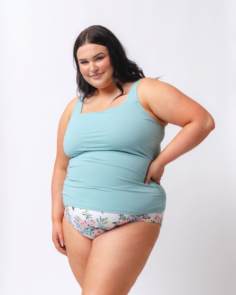 Photo of a woman wearing a light blue square neck swim tankini top and a white and pink floral swim bottom- side angle