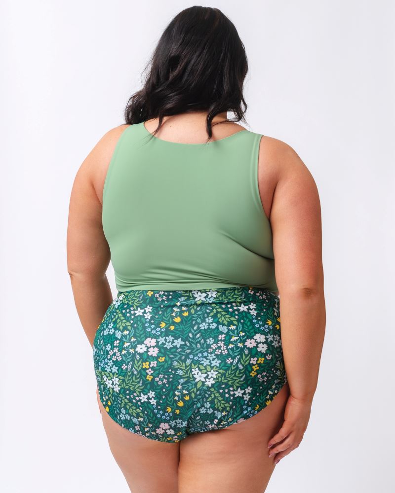 Photo of a woman wearing a light green knotted swim crop top and a dark green floral/ light green reversible swim bottom- floral side- back angle