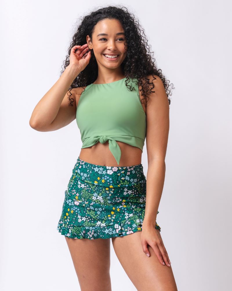 Photo of a woman wearing a light green knotted swim crop top and a  dark green floral swim skirt