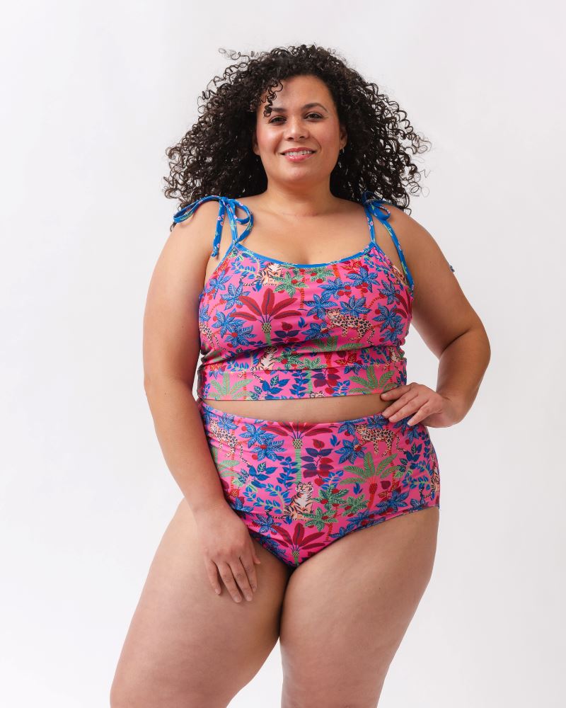 Photo of a woman wearing a bold pink print featuring tigers/ blue and pink floral reversible ultra high waist swim bottoms- tiger side and a matching shoulder-tie swim crop top