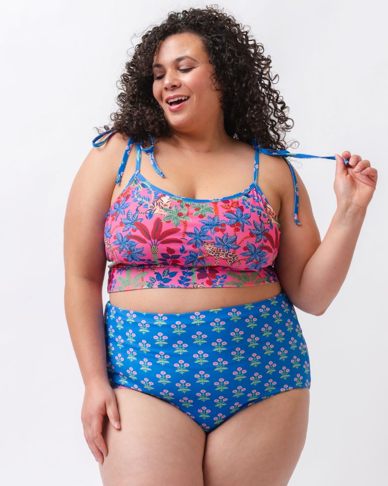 Photo of a woman wearing a bold pink and blue print featuring tigers and leopards shoulder-tie swim crop top and a bold pink print featuring tigers and leopards/ blue floral reversible swim bottom- floral side