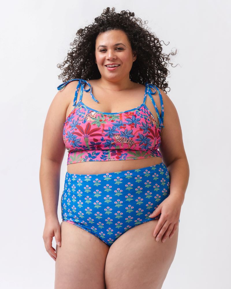 Photo of a woman wearing a bold pink print featuring tigers/ blue and pink floral reversible ultra high waist swim bottoms- floral side and a bold pink print featuring tigers shoulder-tie swim crop top