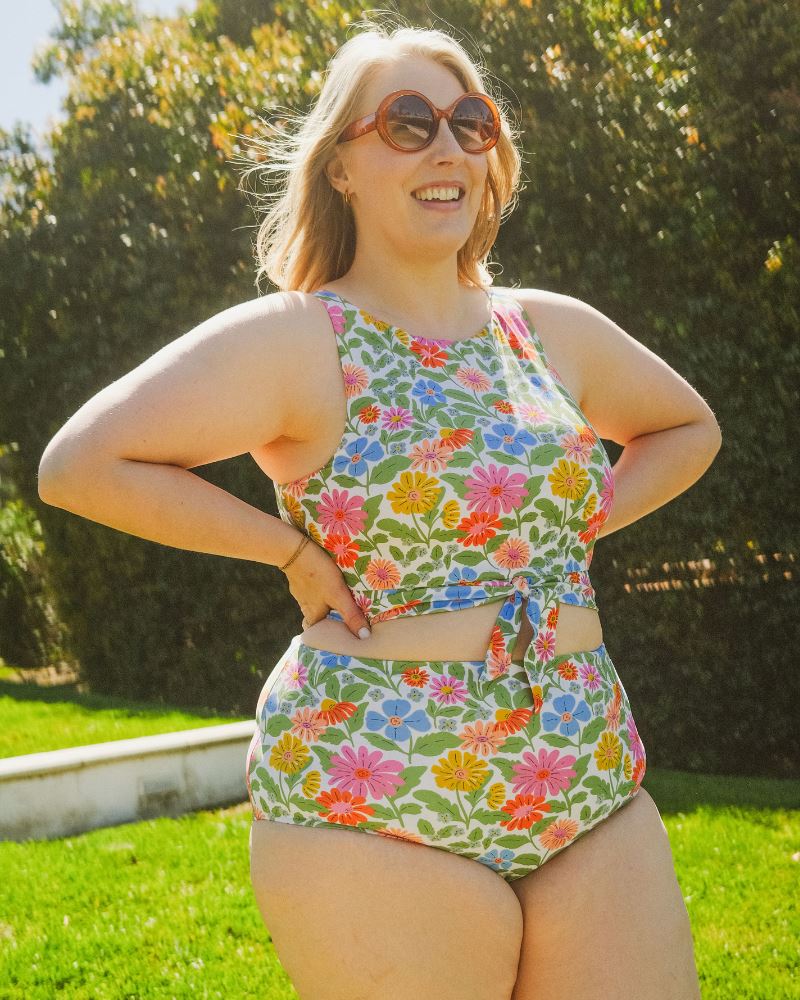 Photo of a woman with her hands on her hips wearing a multi color floral cropped swim top with multi color floral high waist swim bottoms