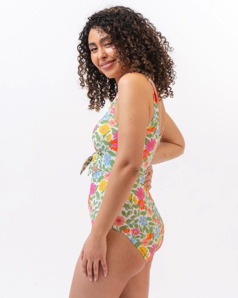 Photo of a woman from the side wearing a multi colored floral knotted one piece swim suit