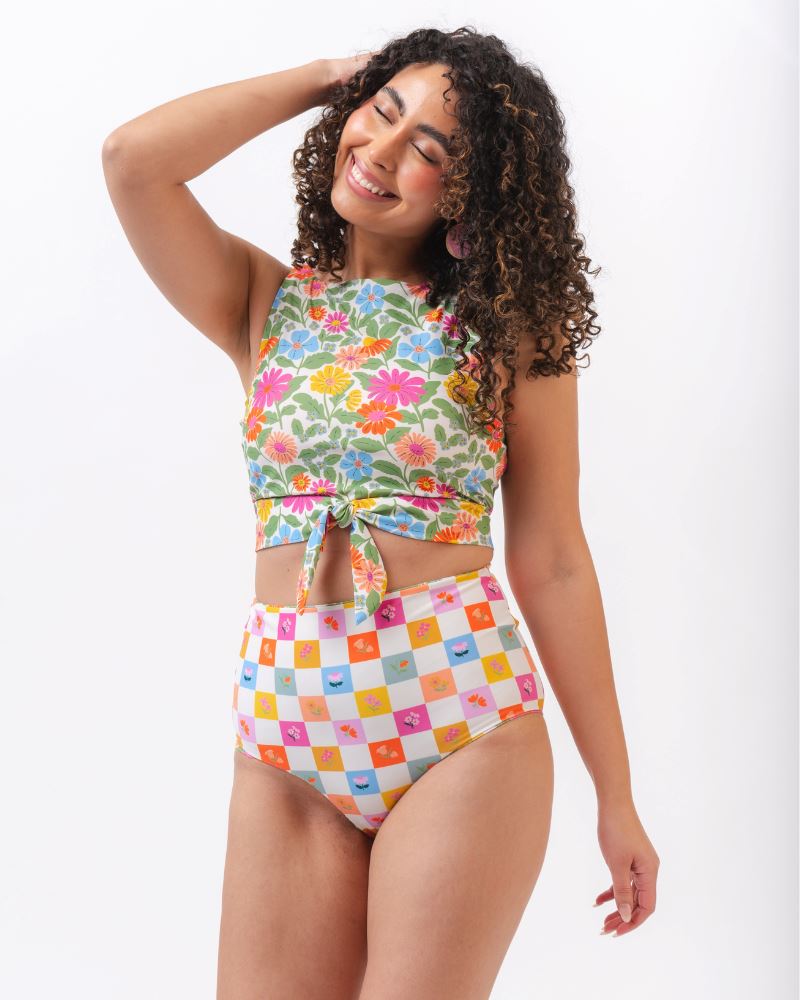 Photo of a woman wearing a multi colored floral cropped swim top with multi colored checkered high waist swim bottoms