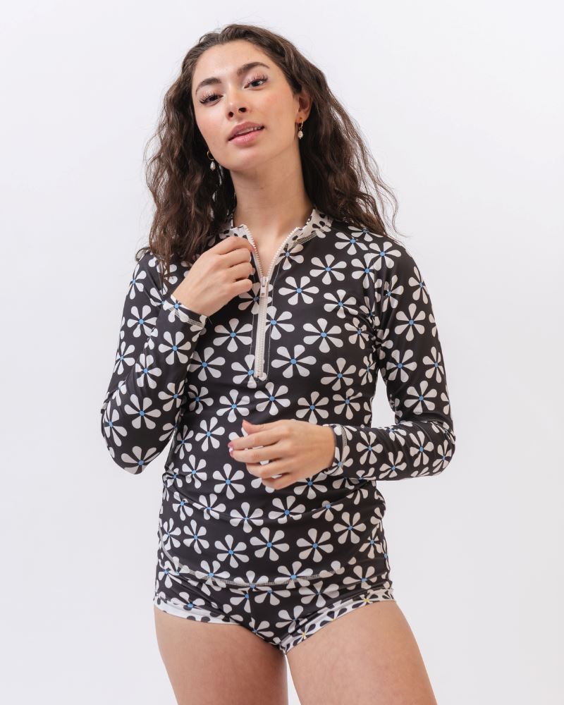 Photo of a woman wearing a black and white floral rash guard swim top and a black and white floral swim bottom