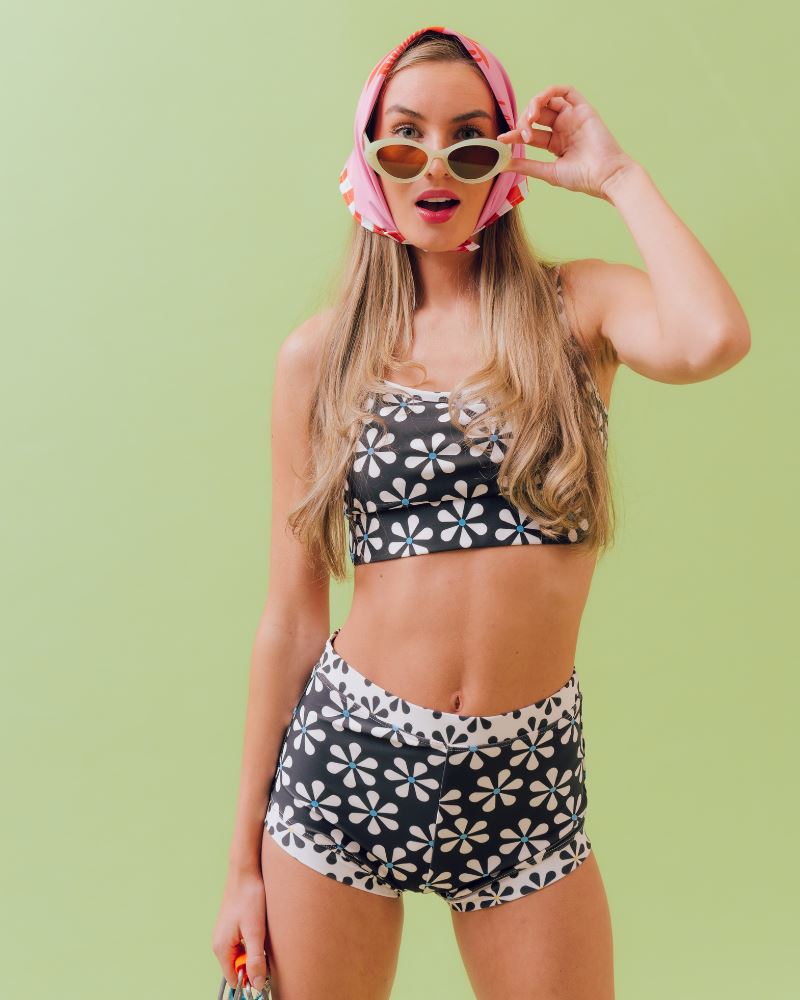 Photo of a woman wearing a pink and red floral bandanna in her hair and a black and white floral swim bottom with a black and white floral swim bralette