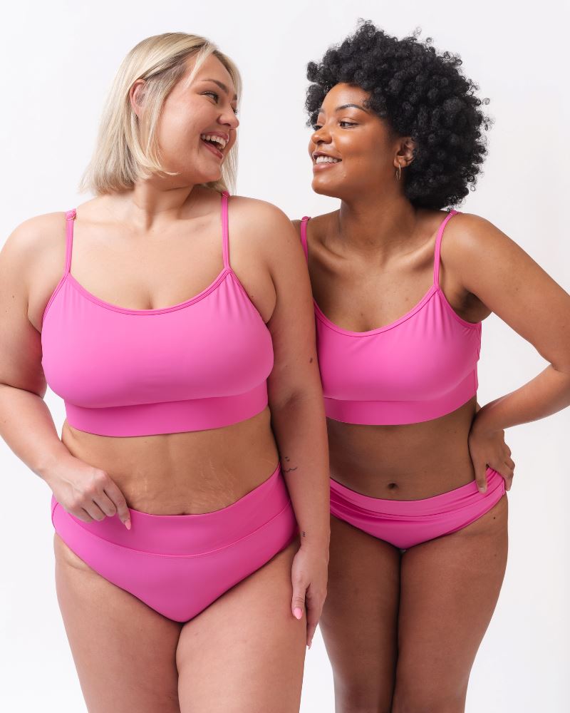 Photo of two women wearing dark pink swim bralettes and dark pink swim bottoms