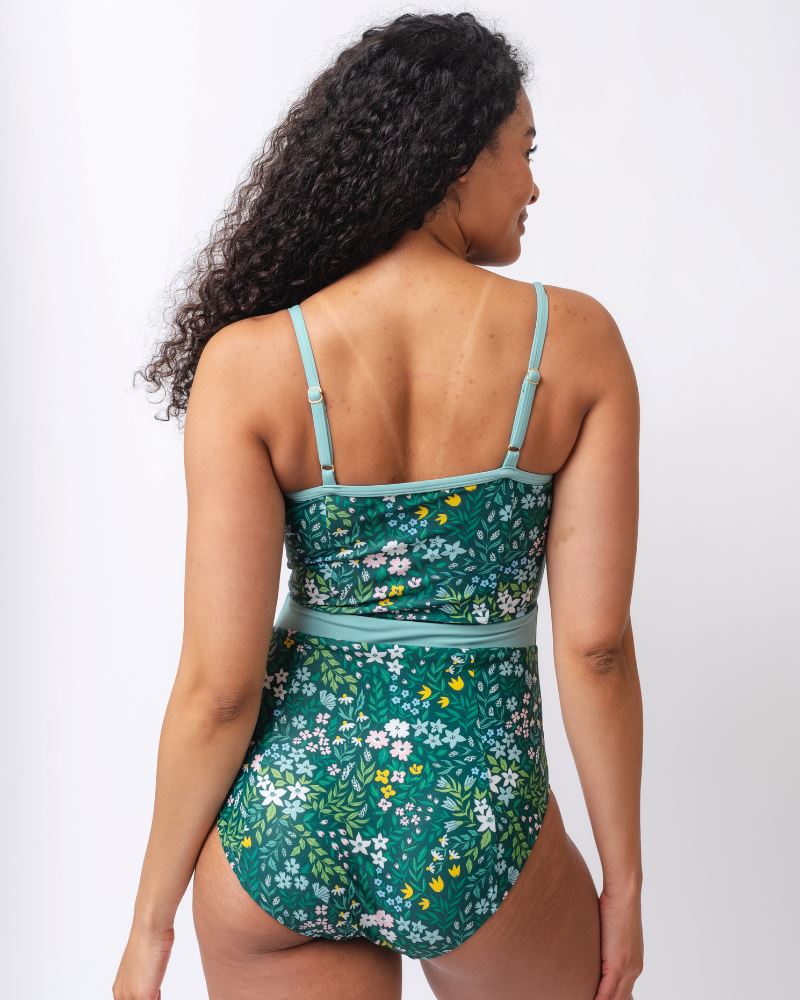 Photo of a woman wearing a dark green floral classic one-piece swimsuit- back angle