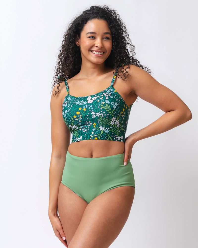 Photo of a woman wearing a dark green floral/ light green reversible swim bottom - light green side and a dark green floral shoulder-tie swim crop top