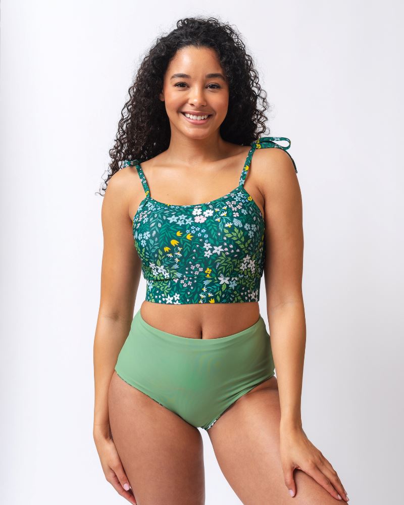 Photo of a woman wearing a dark green floral shoulder-tie swim crop top and a dark green floral/ light green reversible swim bottom- light green side