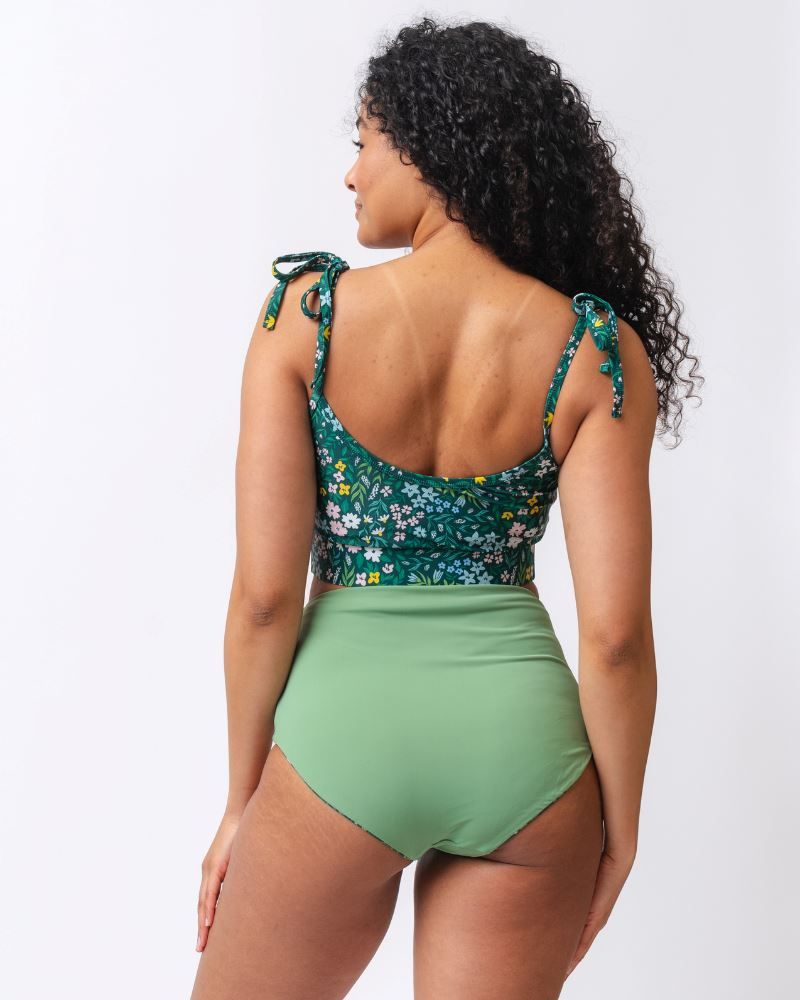 Photo of a woman wearing a dark green floral/ light green reversible swim bottom - light green side and a dark green floral shoulder-tie swim crop top- back angle