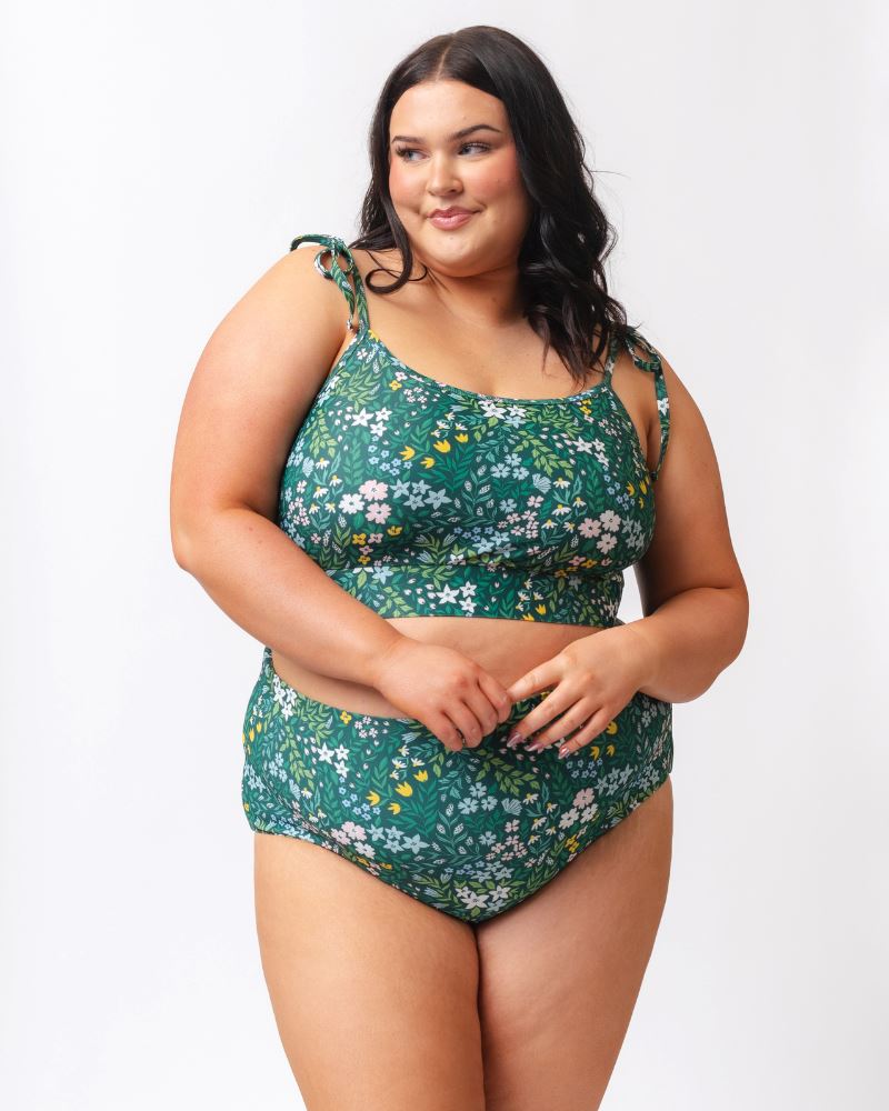Photo of a woman wearing a dark green floral shoulder-tie swim crop top and a dark green floral/ light green reversible swim bottom- floral side