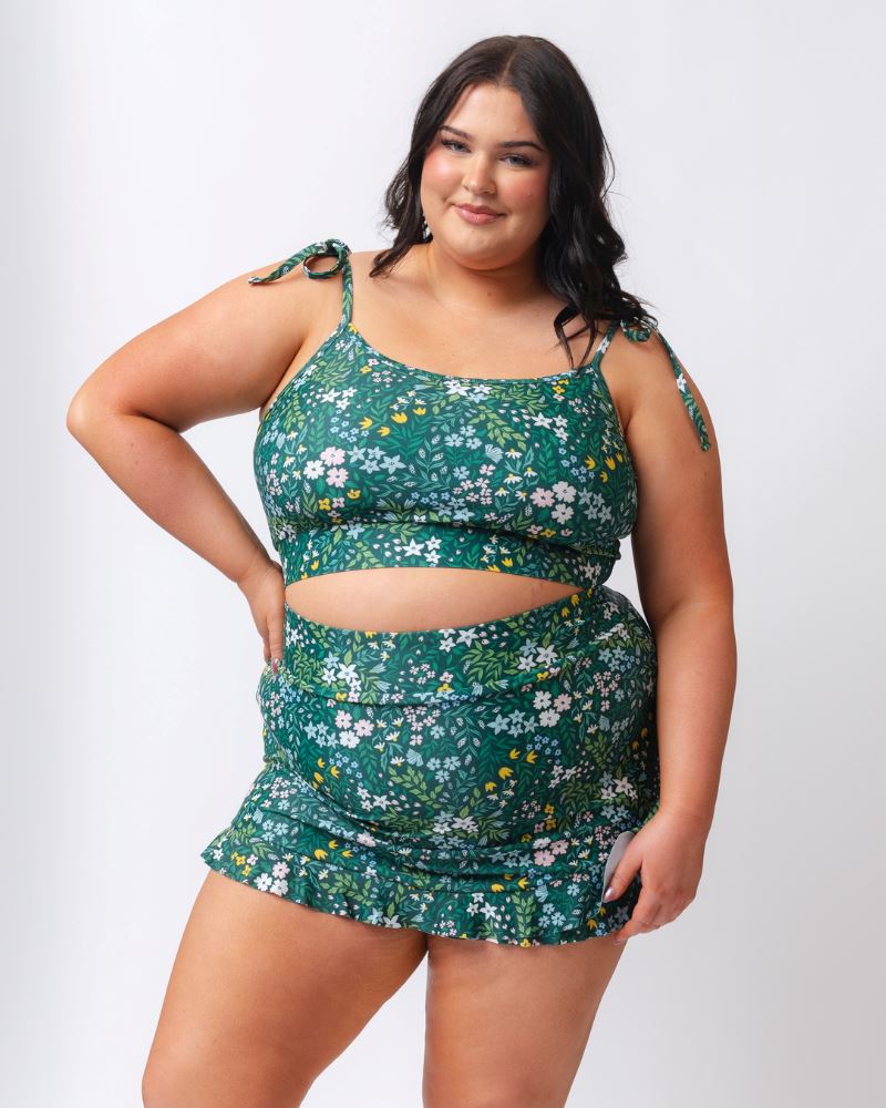 Photo of a woman wearing a dark green floral swim skirt and a dark green floral shoulder-tie swim crop top