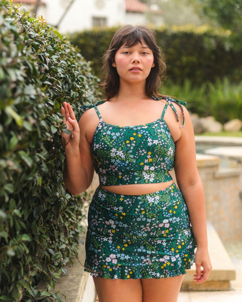 Photo of a woman wearing a dark green floral swim skirt and a dark green floral shoulder-tie swim crop top