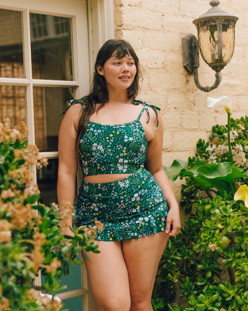 Photo of a woman wearing a dark green floral shoulder-tie swim crop top and a dark green floral swim skirt