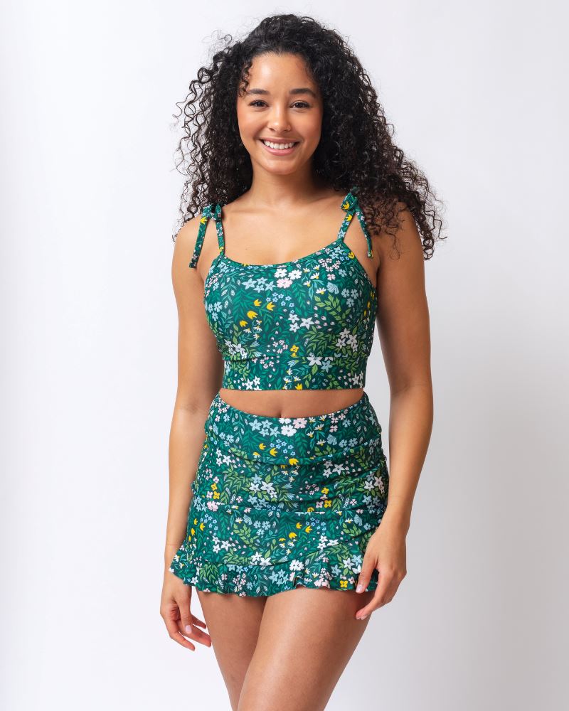 Photo of a woman wearing a dark green floral swim skirt and a dark green floral shoulder-tie swim crop top