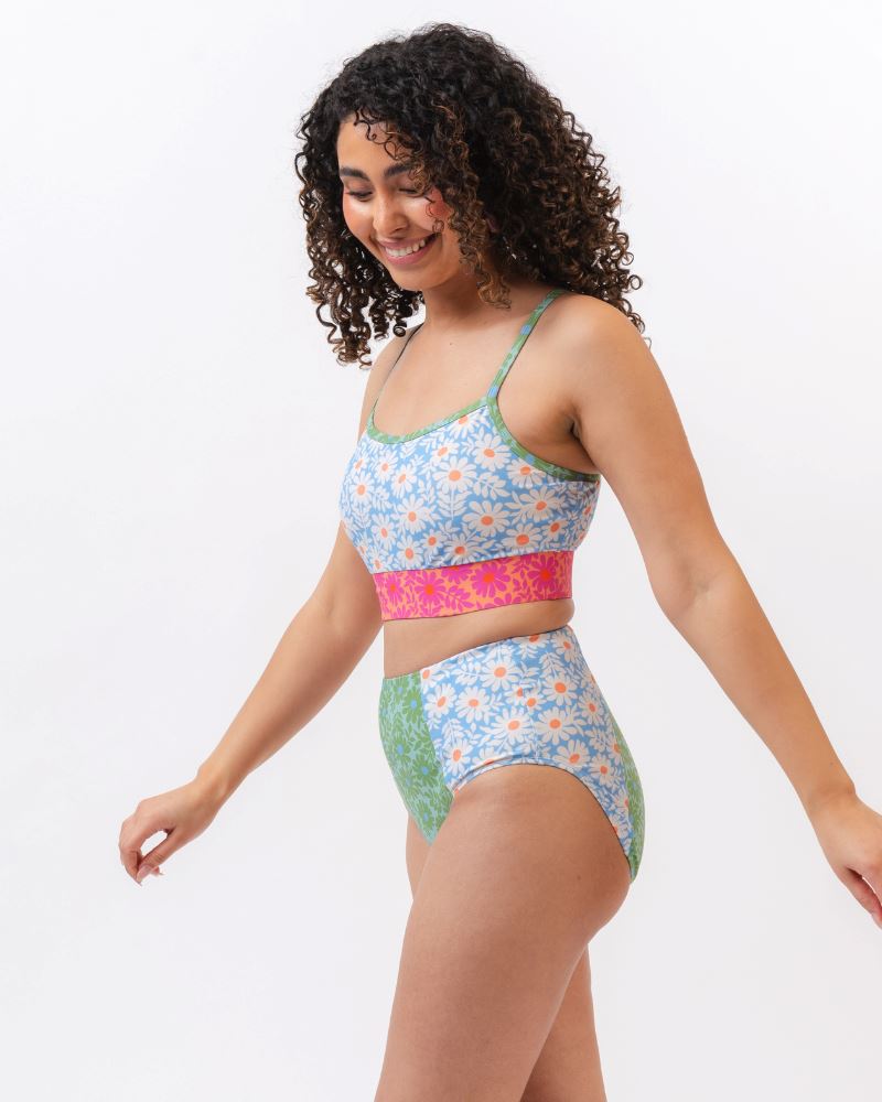 Photo of a woman from the side wearing a blue and pink floral cropped swim top with blue and green floral high waist swim bottoms