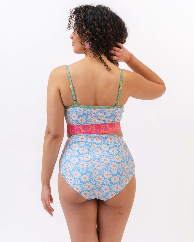 Photo of a woman with her back facing us wearing a blue and pink floral cropped swim top with blue floral high waist reversible swim bottoms