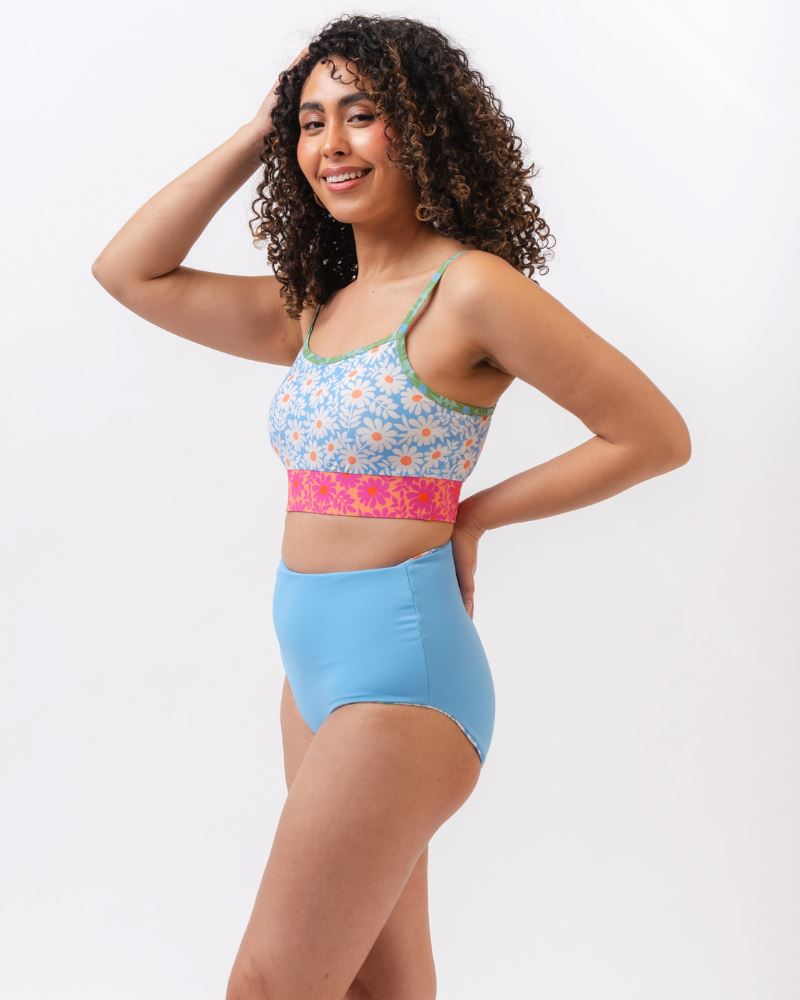 Photo of a woman from the side wearing a blue and pink floral cropped swim top with blue high waist reversible swim bottoms