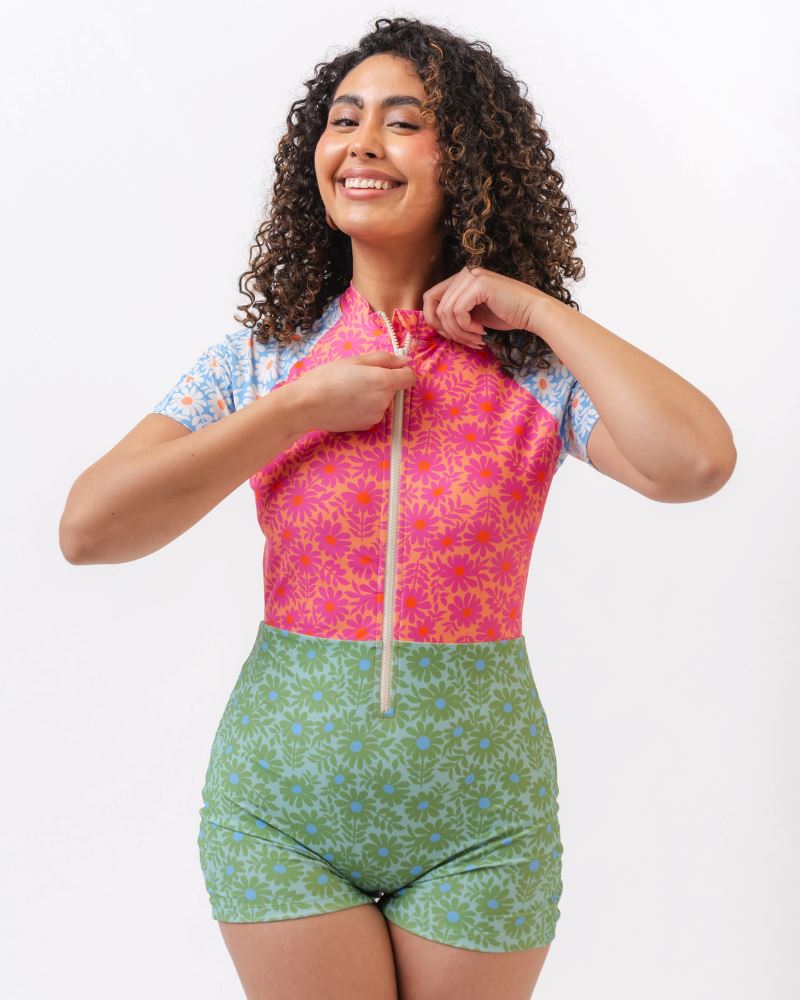 Photo of a woman wearing a blue, pink, and green floral one piece swim suit with short sleeves and attached shorts