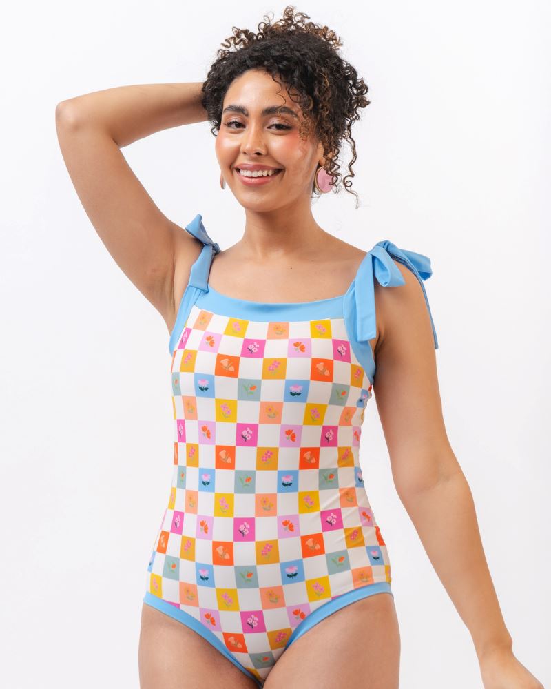 Photo of a woman wearing a multi colored checkered print one piece swim suit with blue straps