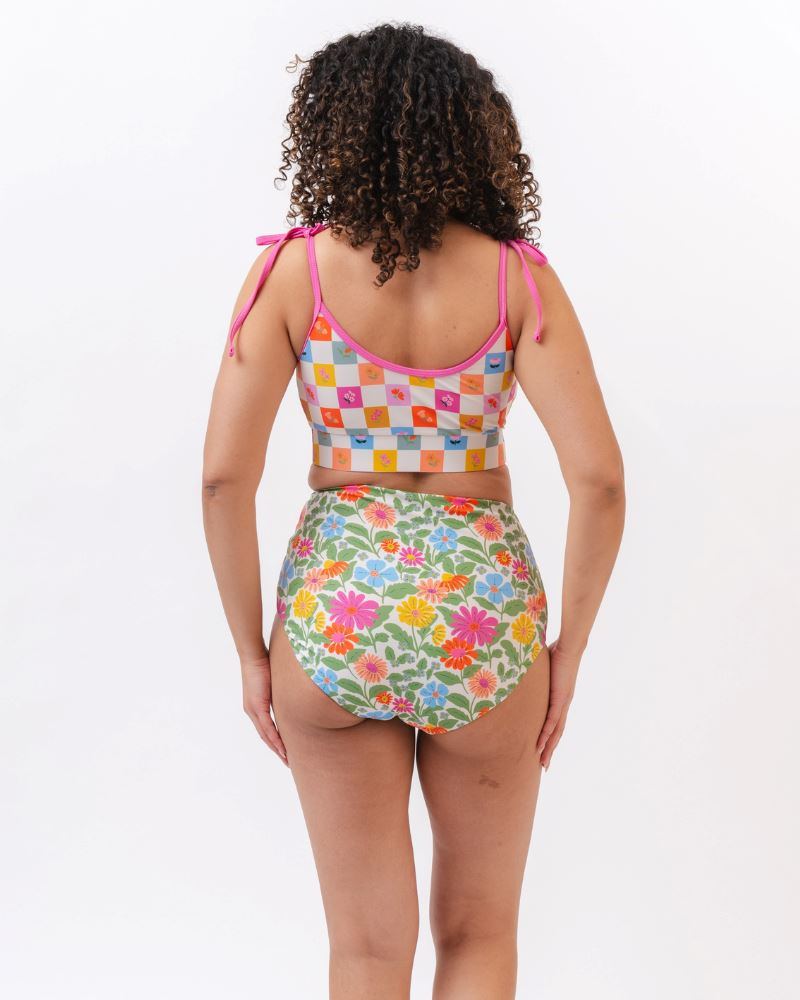 Photo of a woman with her back facing us  wearing a multi colored checkered print cropped swim top with multi colored floral high waist swim bottoms