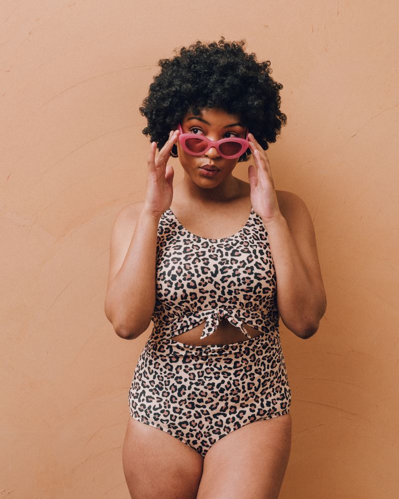 Photo of a woman wearing a leopard print one piece swimsuit with pink sunglasses