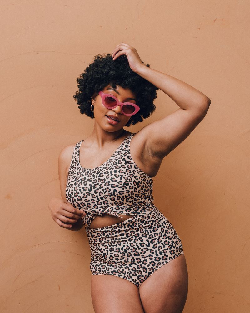 Photo of a woman wearing a leopard print one piece swimsuit with pink sunglasses