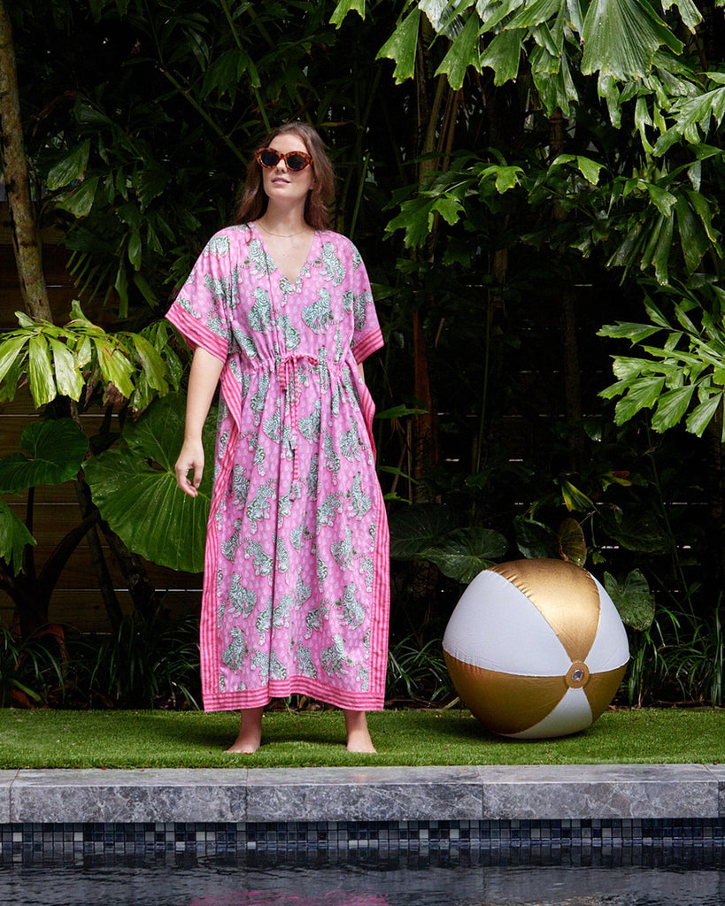 Photo of a woman standing by the pool wearing a bold pink and green tiger print long cover up
