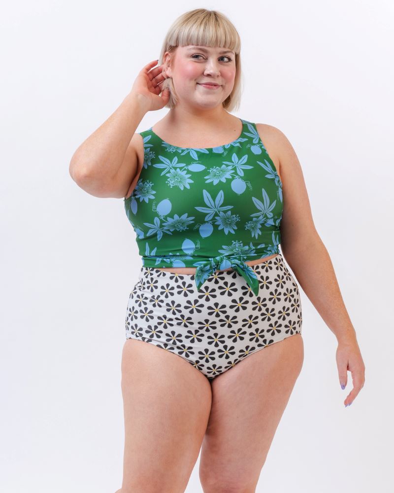 Photo of a woman wearing a green and blue floral/ white and black floral reversible swim bottom (white and black floral side) and a green and blue floral swim crop top