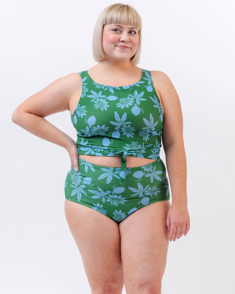 Photo of a woman wearing a green and blue floral/ white and black floral reversible swim bottom (green and blue floral side) and a green and blue floral swim crop top