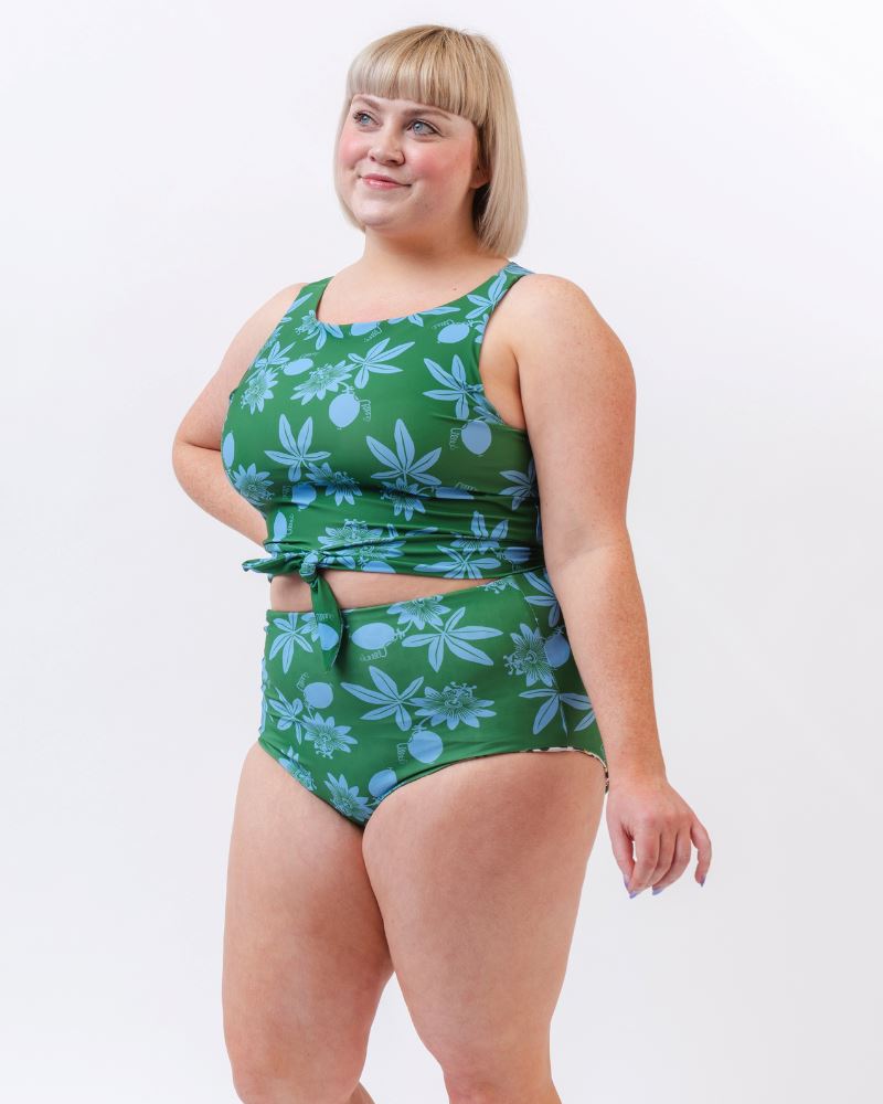 Photo of a woman wearing a green and blue floral/ white and black floral reversible swim bottom (green and blue floral side) and a green and blue floral swim crop top- side angle
