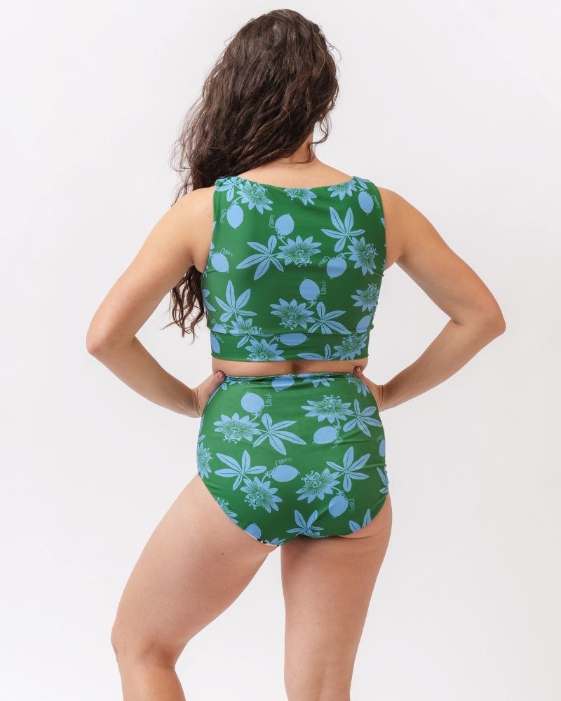 Photo of a woman wearing a green and blue floral/ white and black floral reversible swim bottom (green and blue floral side) and a green and blue floral swim crop top- back angle