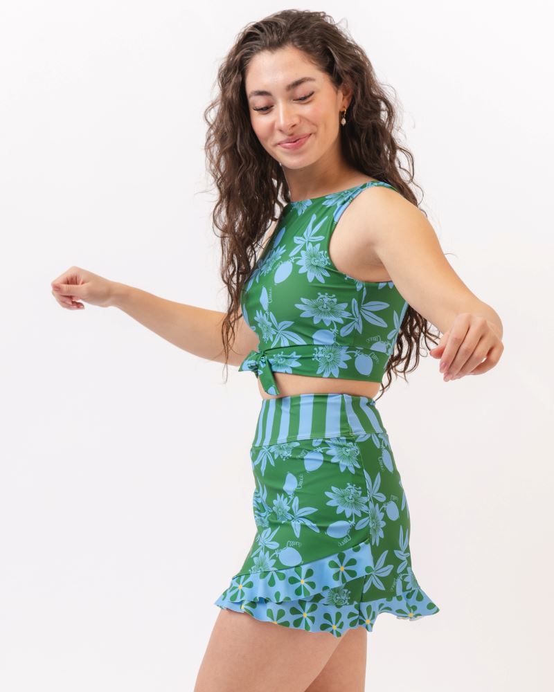 Photo of a woman wearing a green and blue floral swim crop top and a green and blue floral swim skirt bottom- side angle