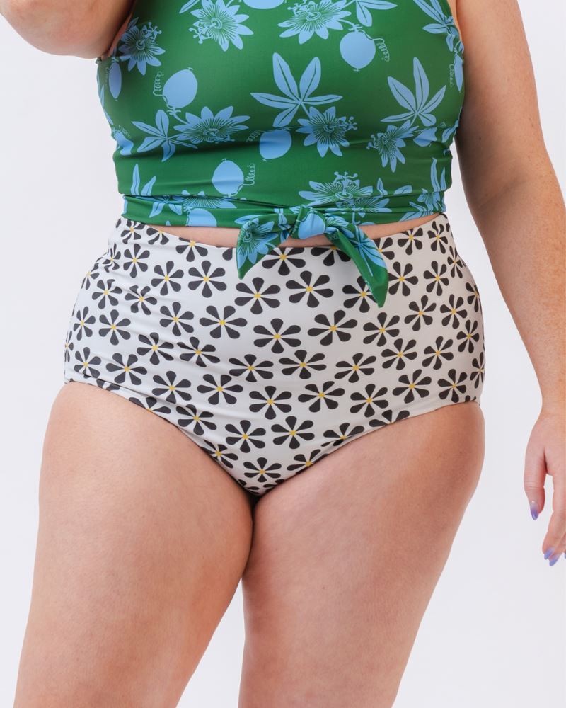 Photo of a woman wearing a green and blue floral/ white and black floral reversible swim bottom (white and black floral side) and a green and blue floral swim crop top