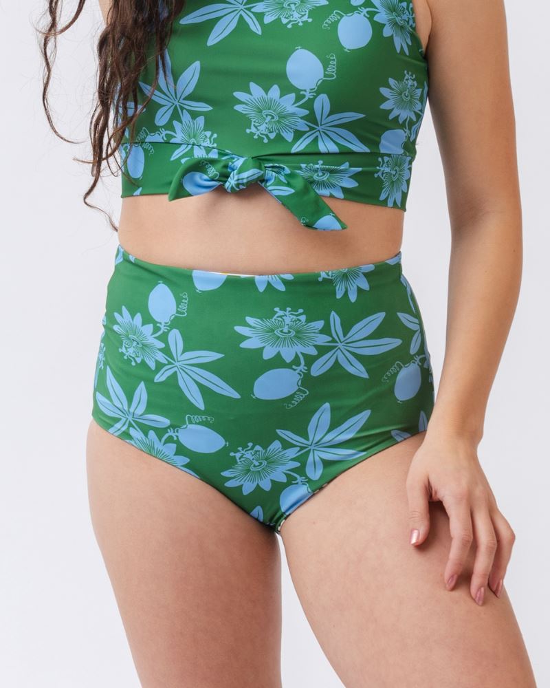 Photo of a woman wearing a green and blue floral/ white and black floral reversible swim bottom (green and blue floral side) and a green and blue floral swim crop top