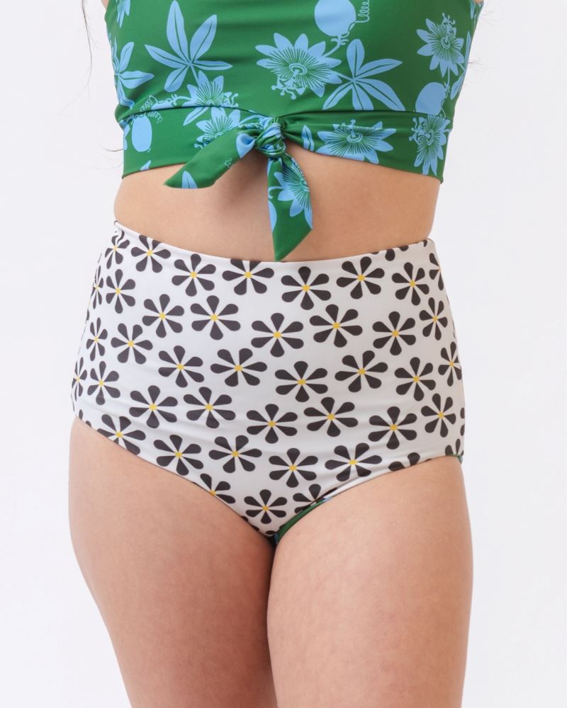 Photo of a woman wearing a green and blue floral/ white and black floral reversible swim bottom (white and black floral side) and a green and blue floral swim crop top