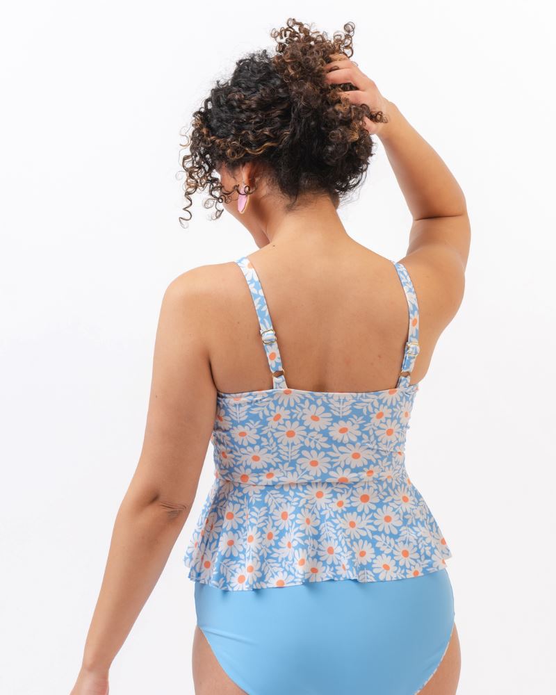 Photo of a woman with her back facing us wearing a blue floral tankini swim top with light blue high waist swim bottoms