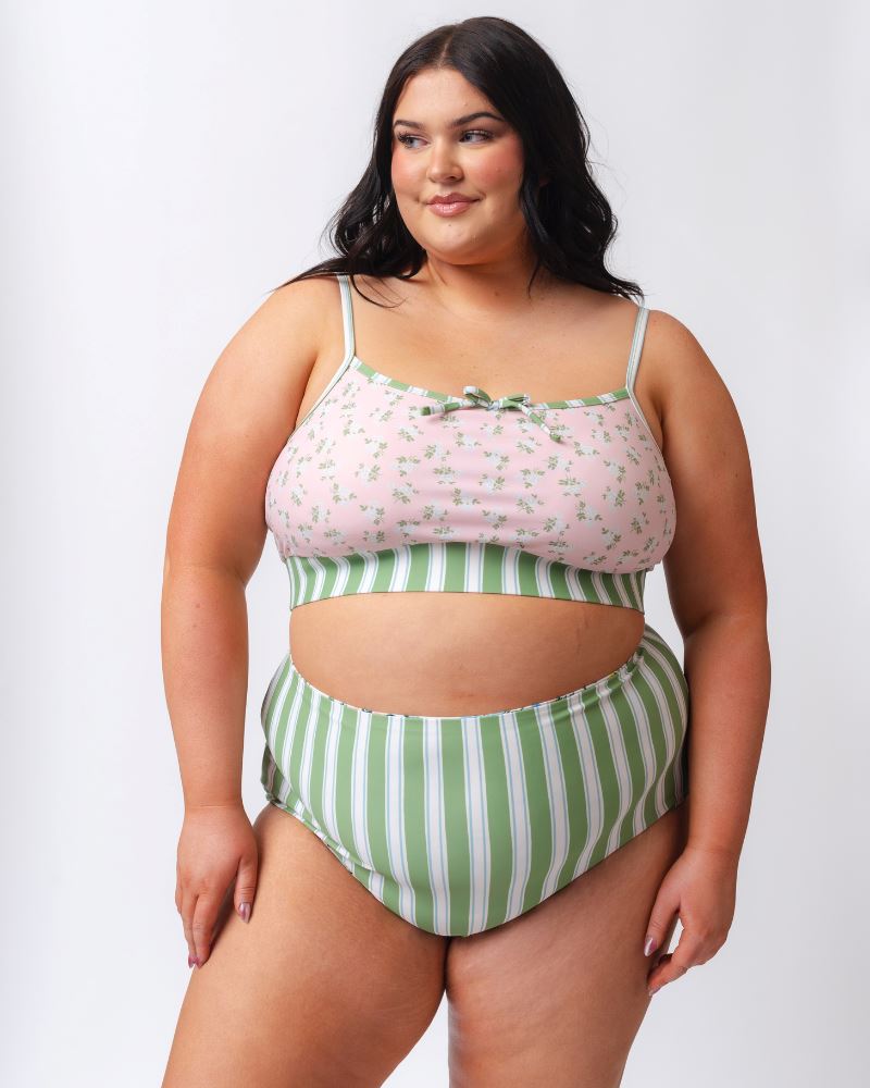 Photo of a woman wearing a pink floral cropped swim top with green and white striped high waist swim bottoms