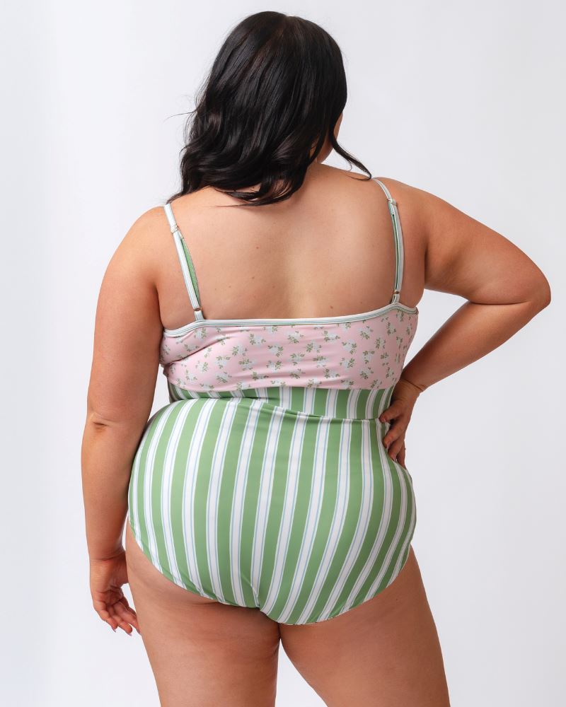 Photo of a woman wearing a pink and green floral swim bralette and a white and pink floral/ green striped reversible swim bottom- striped side- back angle