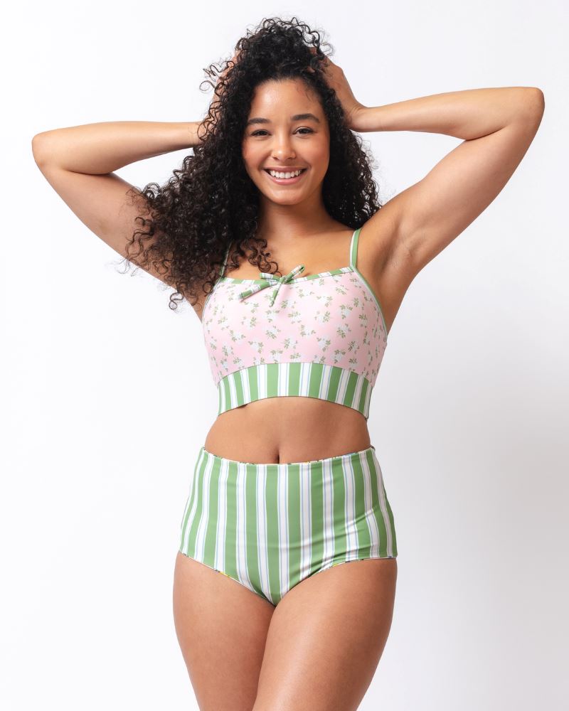 Photo of a woman wearing a pink floral cropped swim top with green and white striped high waist swim bottoms